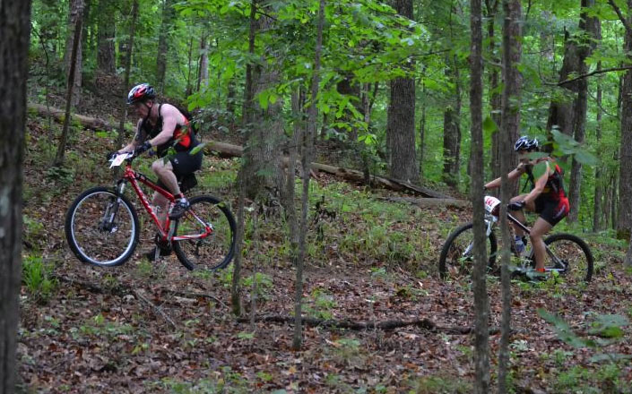 Photo of two individuals riding their bikes through a trail.